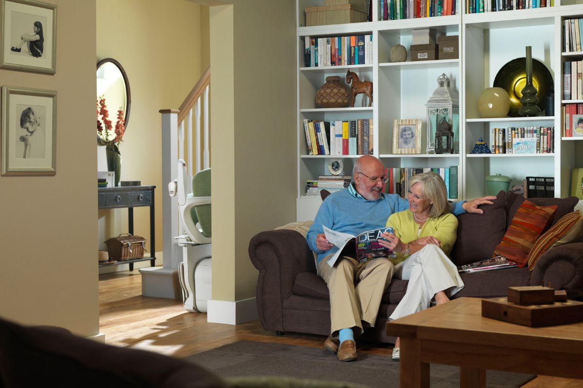 Happy couple resting, with a stairlift installed on the stairs.